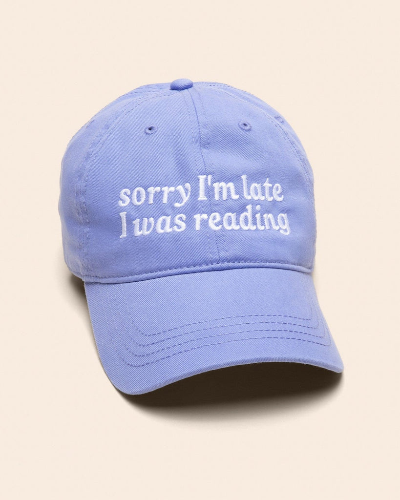 Light blue cap with 'sorry I'm late I was reading' text on a beige background